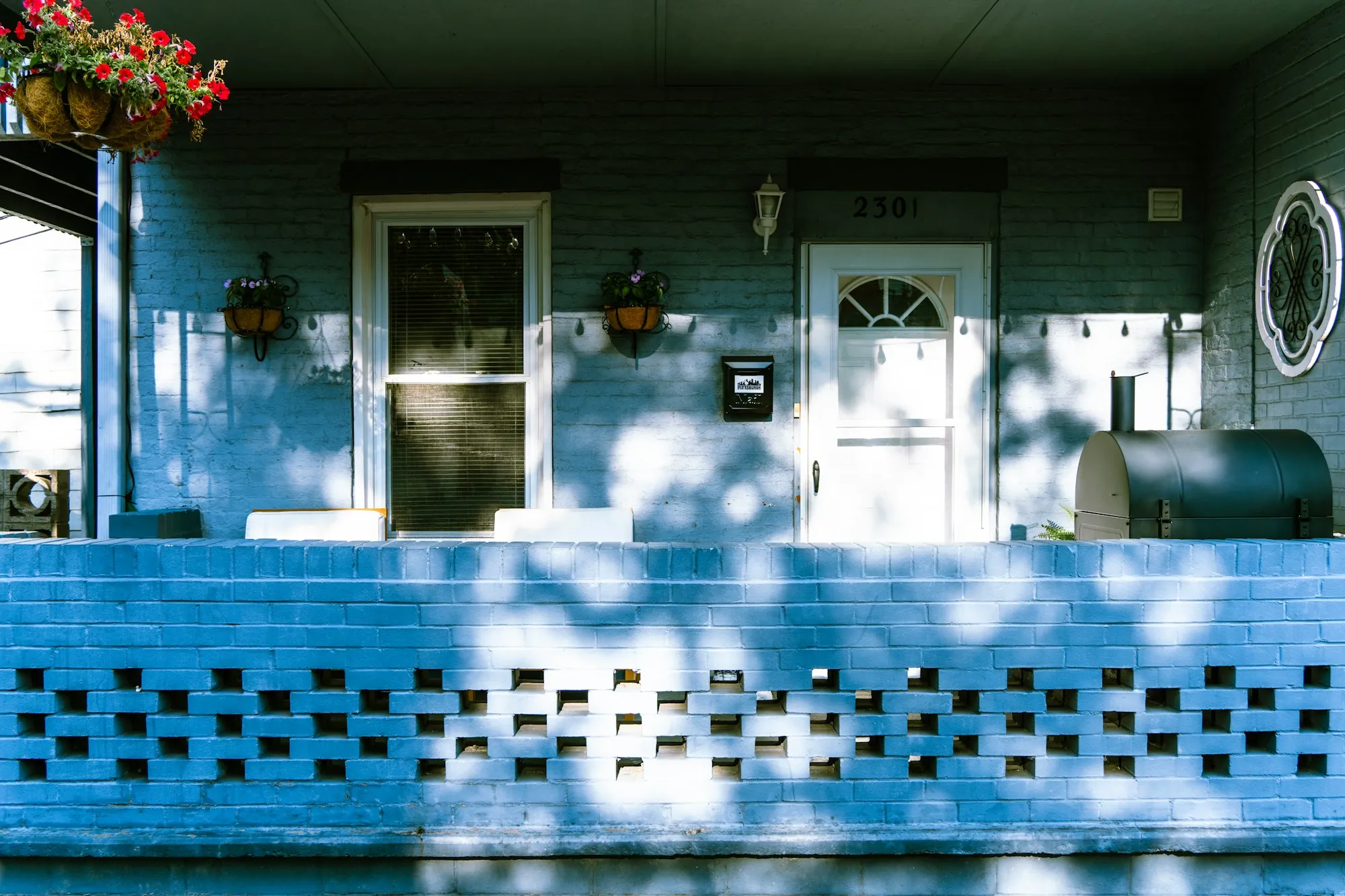 Front porch of a blue house shaded by a tree